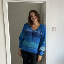 Load image into Gallery viewer, A woman wearing a blue and teal striped knit sweater with a V-neck and long sleeves, standing in a doorway in an indoor setting.