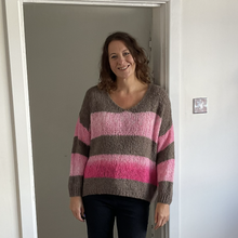 Load image into Gallery viewer, A woman wearing a chunky knit sweater with horizontal stripes in brown, light pink, and magenta, standing in a doorway.