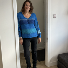 Load image into Gallery viewer, A woman wearing a blue and teal striped knit sweater, black pants, and black boots, standing in a doorway inside a home.