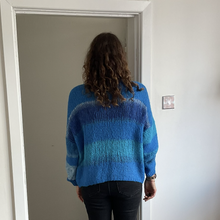 Load image into Gallery viewer, A person viewed from behind wearing a blue striped fuzzy knit sweater and black pants, standing in a doorway in a home interior.