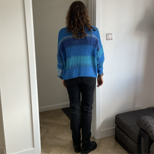 Load image into Gallery viewer, A person viewed from behind wearing a blue striped knit sweater, black jeans, and black boots, standing in a doorway inside a home.
