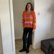 Load image into Gallery viewer, A woman stands in a doorway wearing a bright orange knit sweater with horizontal pink, purple, and yellow stripes, paired with dark jeans and black boots.