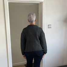 Load image into Gallery viewer, A person viewed from behind wearing a dark charcoal gray knit sweater and dark navy jeans, standing in a doorway inside a home.