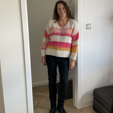 Load image into Gallery viewer, A woman stands in a doorway wearing a cream knit sweater with pink, orange, and yellow horizontal stripes, paired with dark jeans and black boots.
