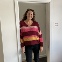 Load image into Gallery viewer, A woman with curly brown hair stands in a doorway wearing a maroon, pink, and yellow striped knit sweater and dark jeans.
