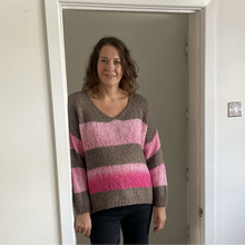 Load image into Gallery viewer, A woman wearing a chunky knit V-neck sweater with horizontal stripes in brown, light pink, and magenta, standing in a doorway.
