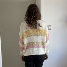 Load image into Gallery viewer, A person viewed from behind wearing a chunky knit sweater with horizontal stripes in cream, mustard yellow, and light pink, paired with dark jeans in an indoor setting.
